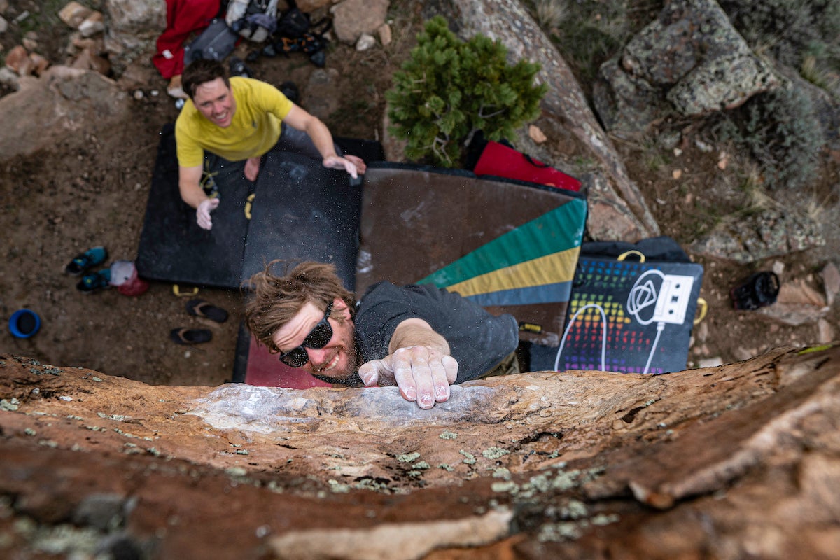 A boulderer grabbing a small hold while his spotter waits below