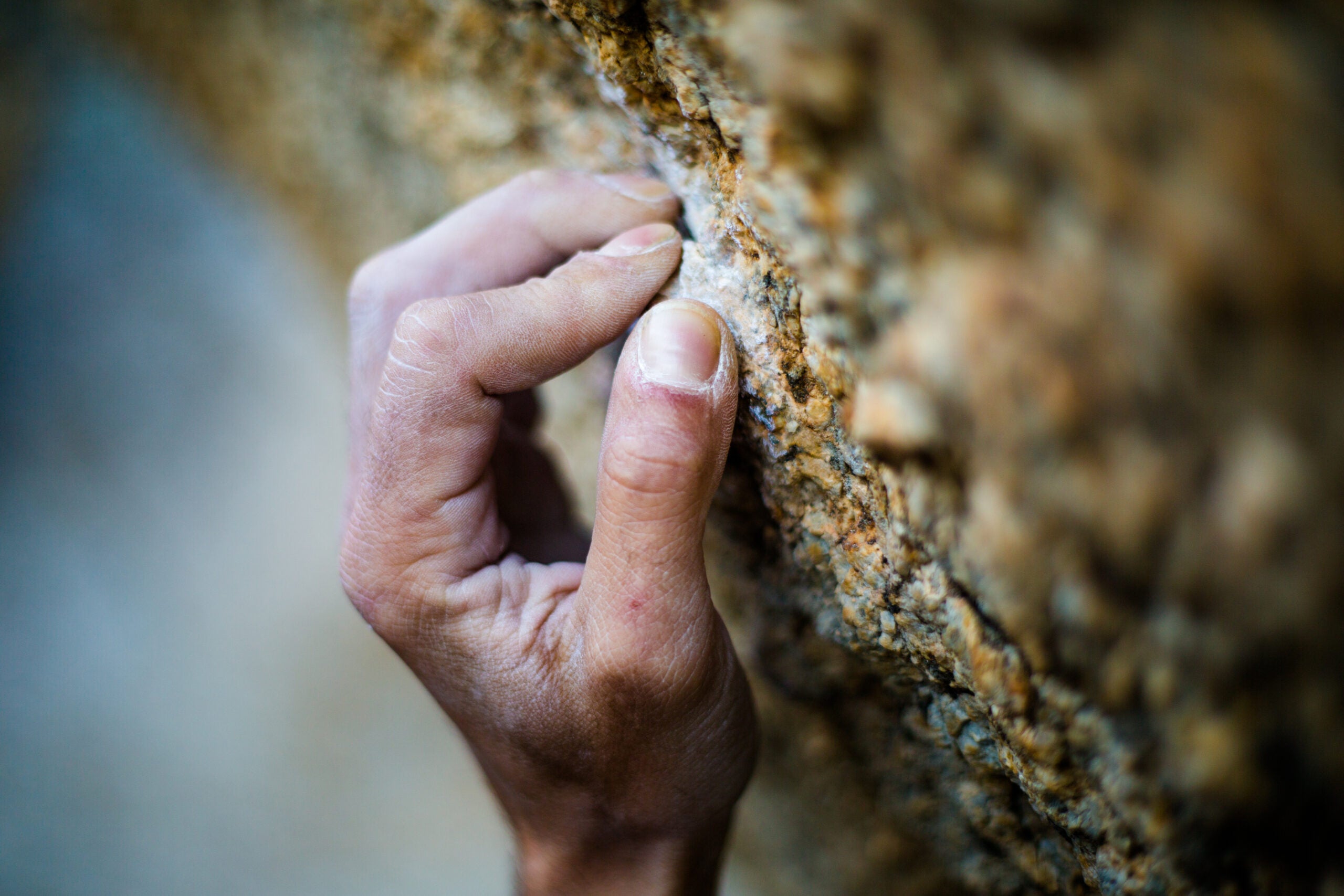 Hand and fingers grasp rough rock while climbing.