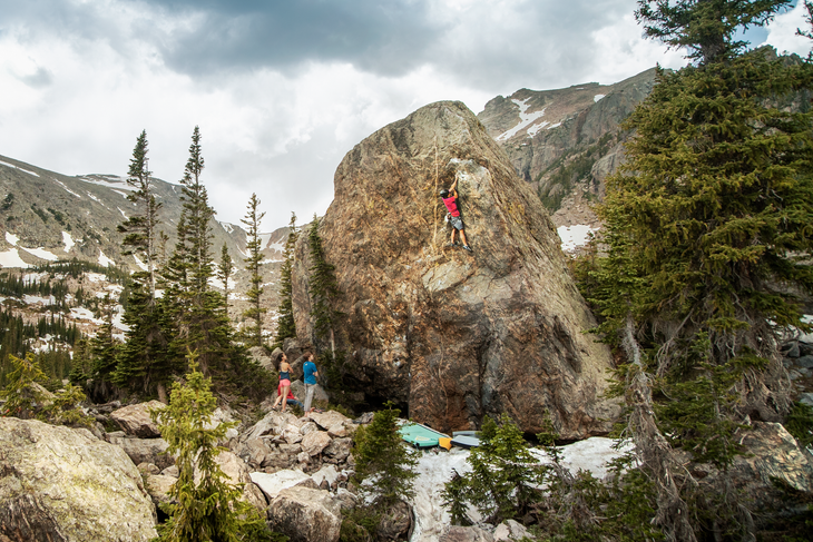 ice ice baby 1 White man in red shirt climbs high on a boulder as his teammates watch from below.