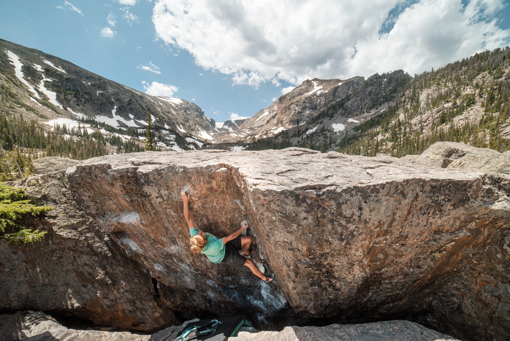 zach gallah Zach Gallah climbs the side of a boulder with mountains in the background.