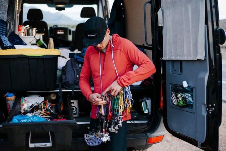 BCAndyB_190225_0011 White man in black hat and red Pentapitch hoodie organizes climbing gear near the back of a van.
