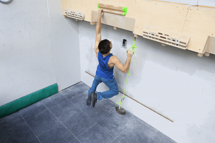 A climber trains on a hang board by doing a one arm dead hang