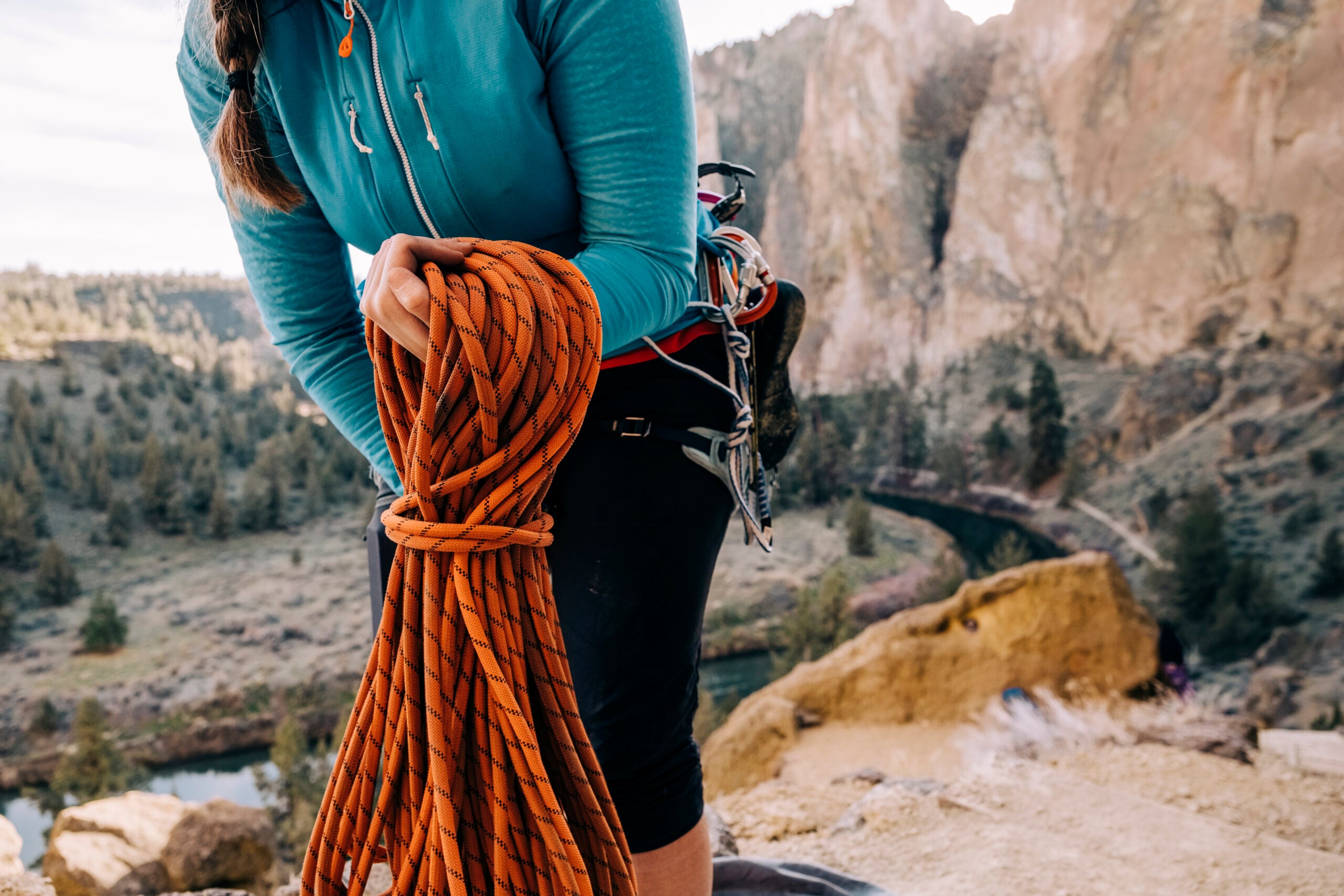 Redmond, OR , USA - December , 02, 2021: Close up detail shot of a female rock climber coils a climbing rope with a dramatic desert mountain view of Smith Rock State Park in the background on December 2, 2021.