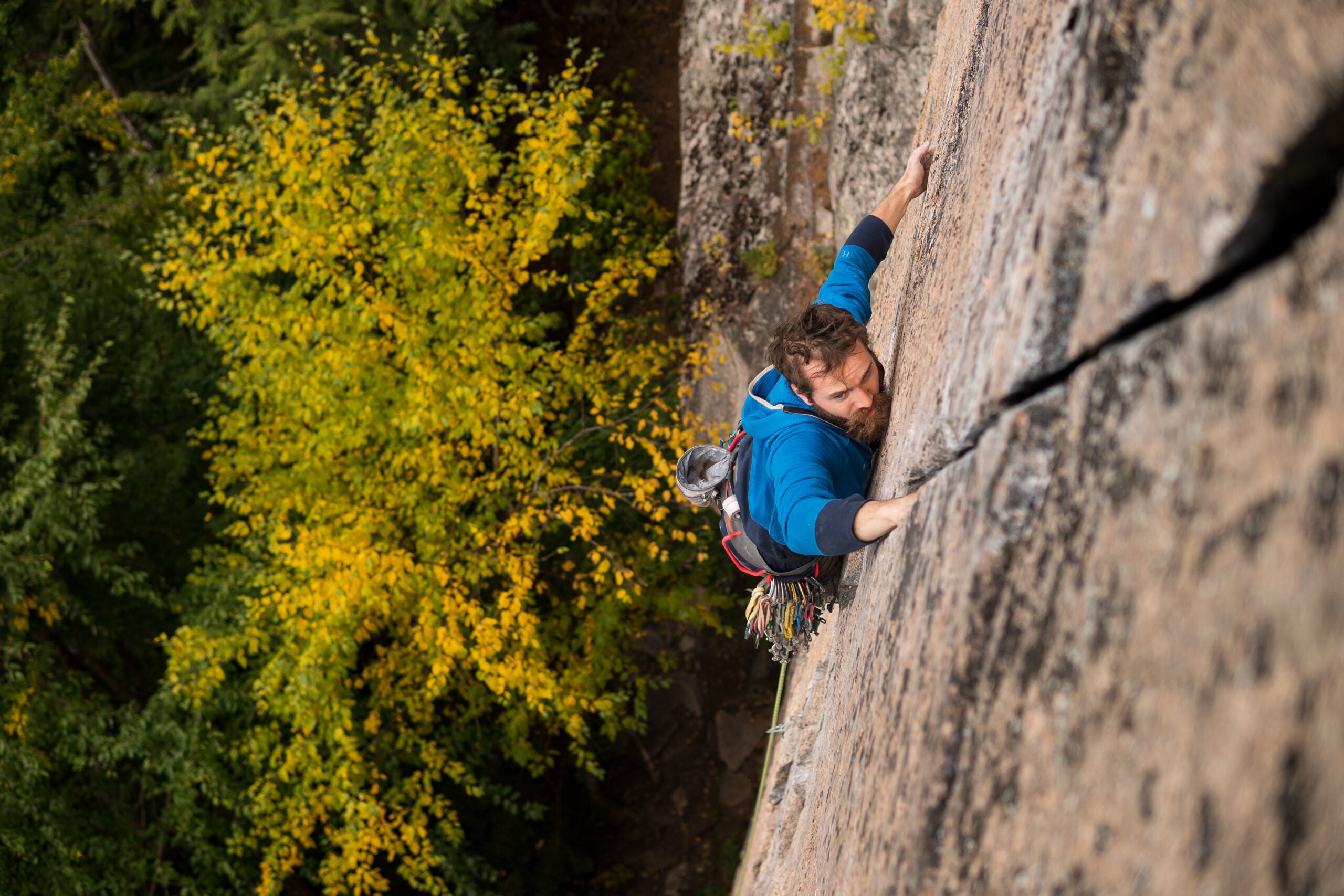 A climber in a blue sweatshirt climbing a wide hands crack.