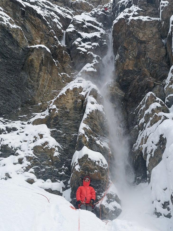 Climbers stands below steep mountain face. 