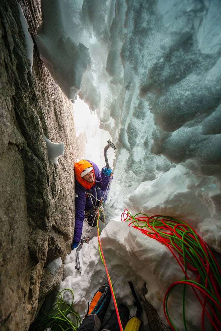 Alpinist climbs into steep snow cave on Alaskan mountain.