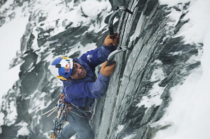 Man ice climbs up mountain face.