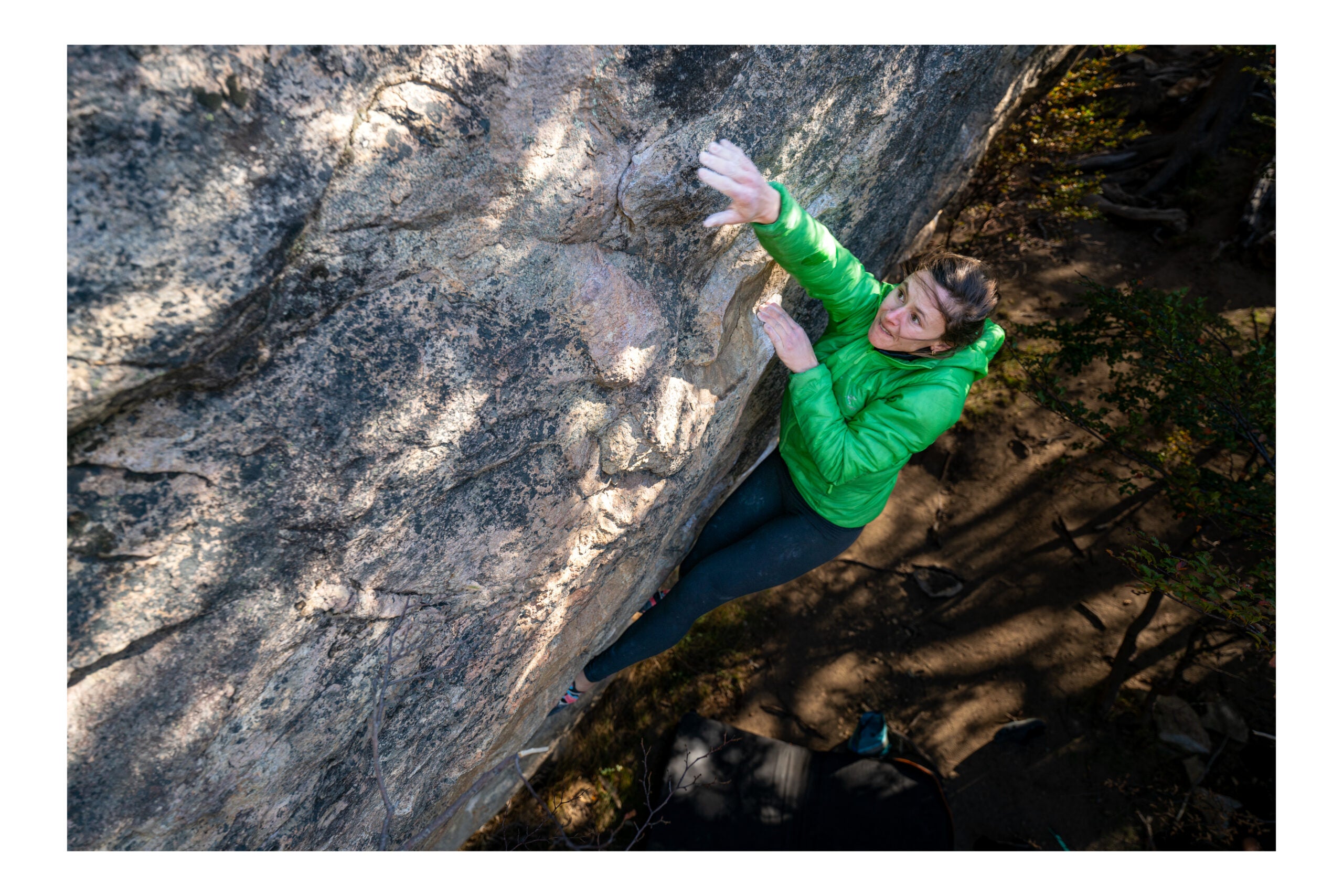 A woman in a green jacket bouldering