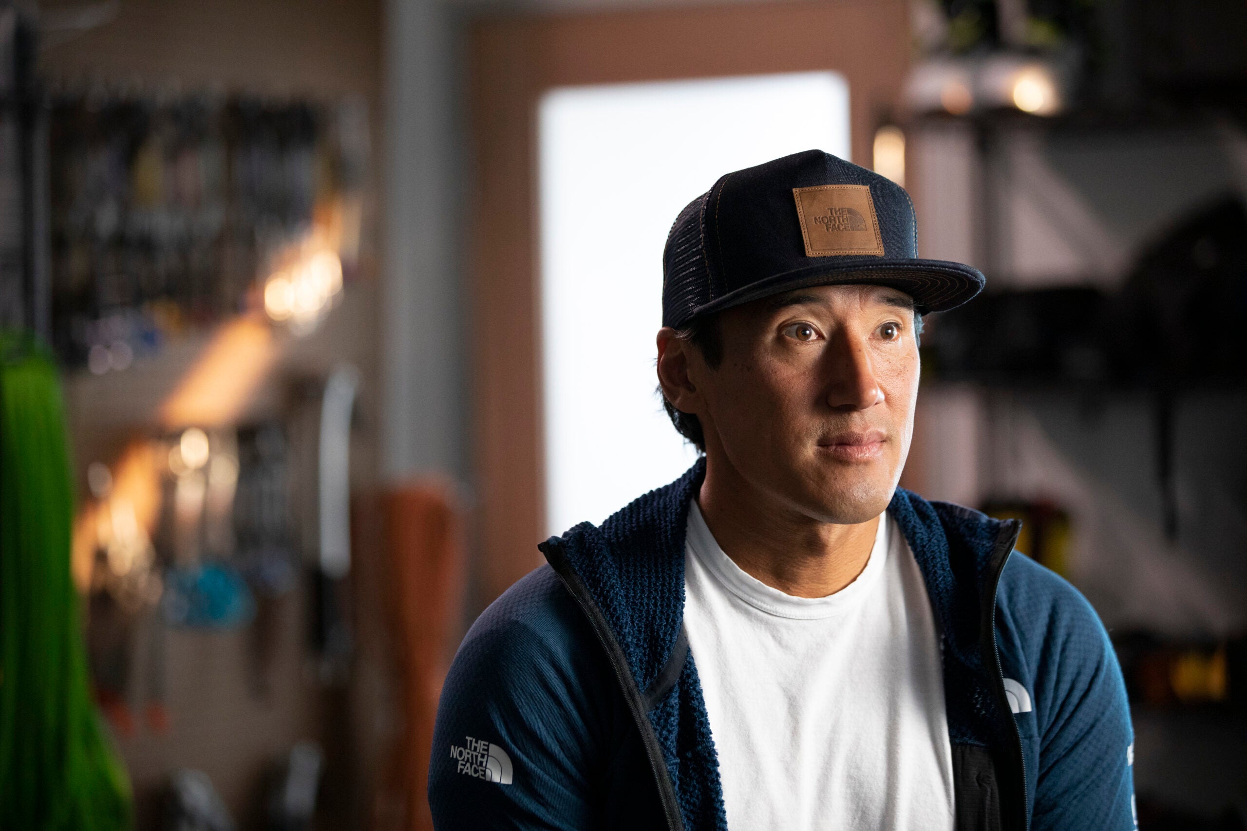 Jimmy Chin wearing a ballcap, white t-shirt, and blue North Face fleece, interview inside.