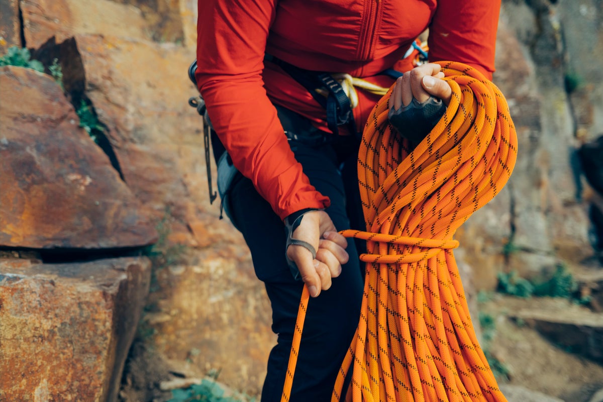 Mountain climber coils a orange climbing rope and ties it off in preparation for putting it in a