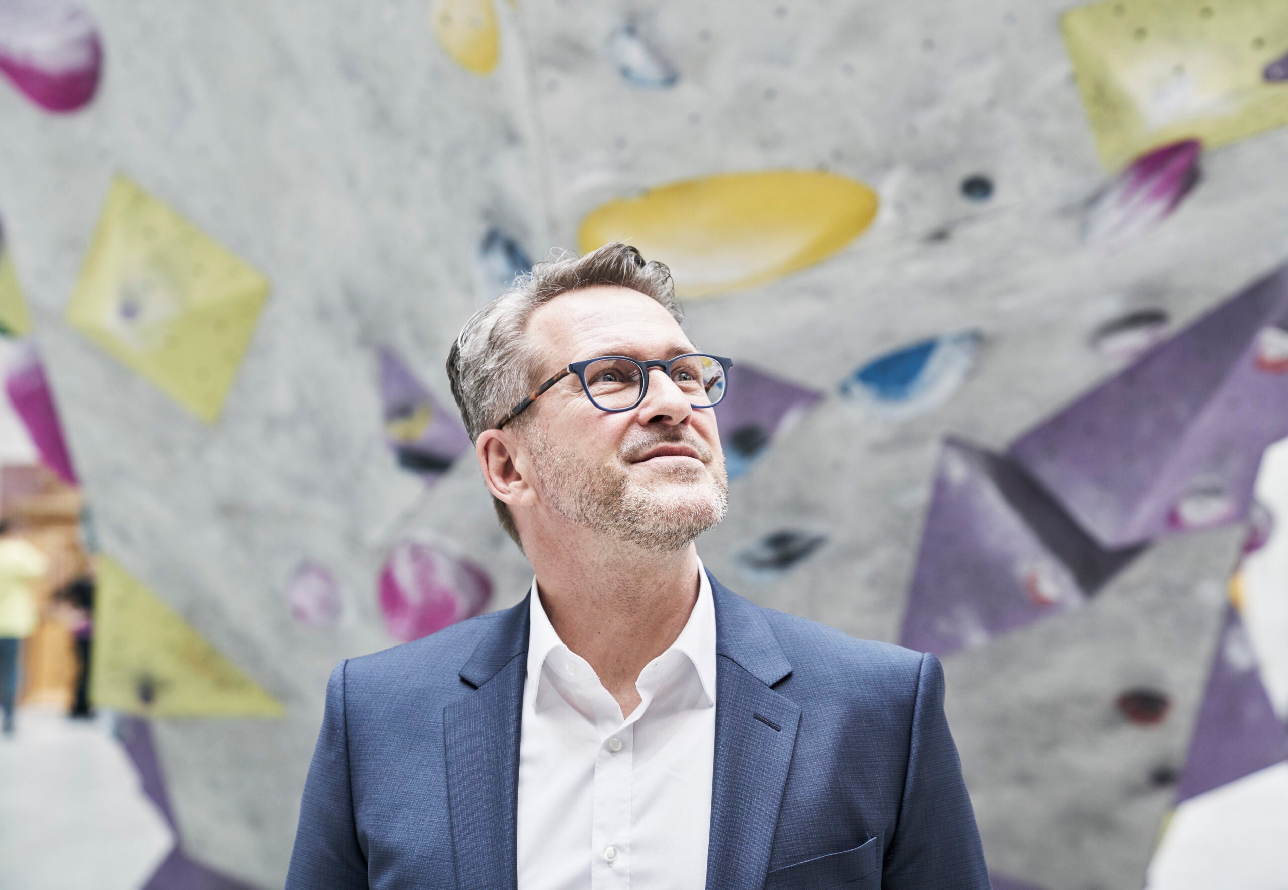Portrait of smiling businessman in front of a sparsely set climbing wall.