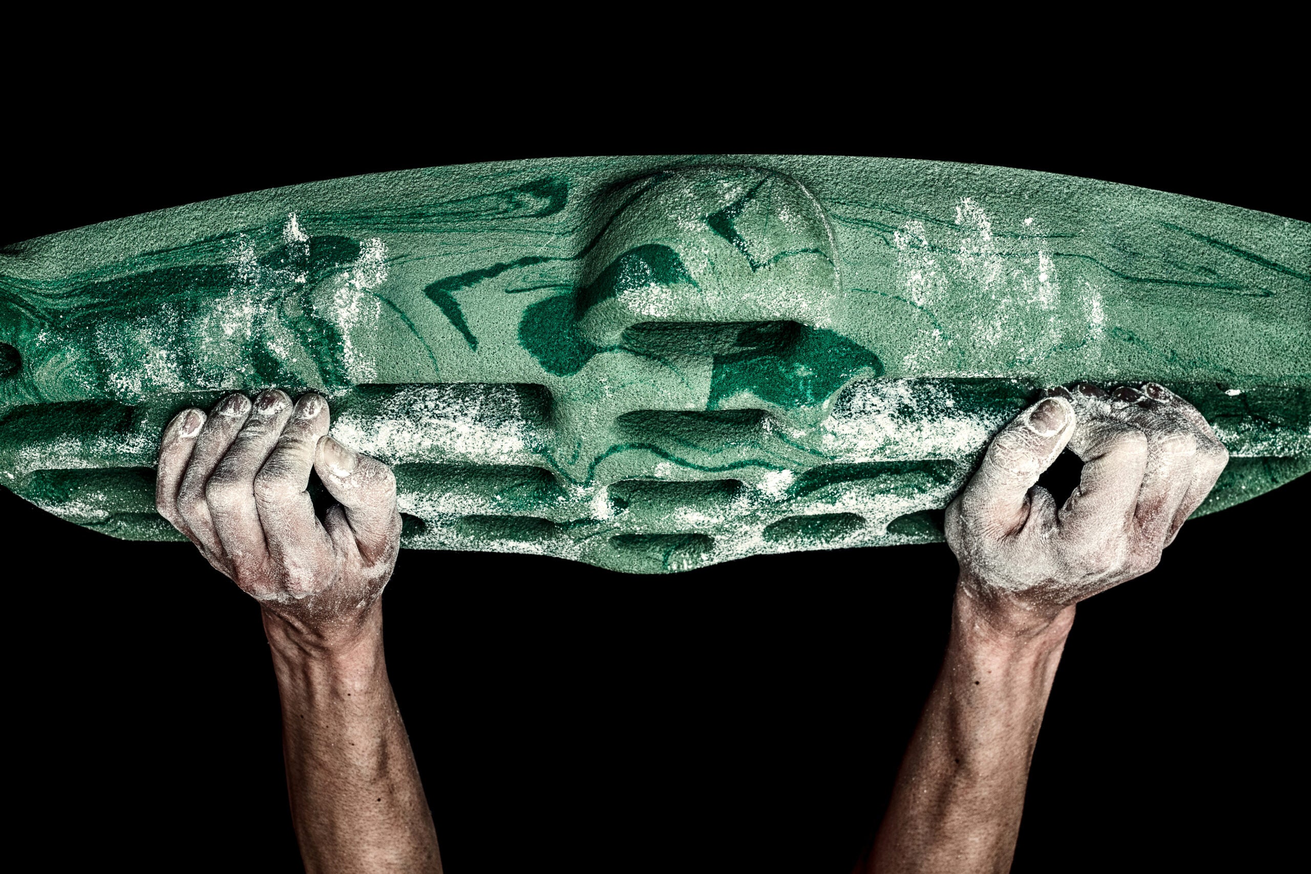 A close up of a climber's hands on a green and black fingerboard