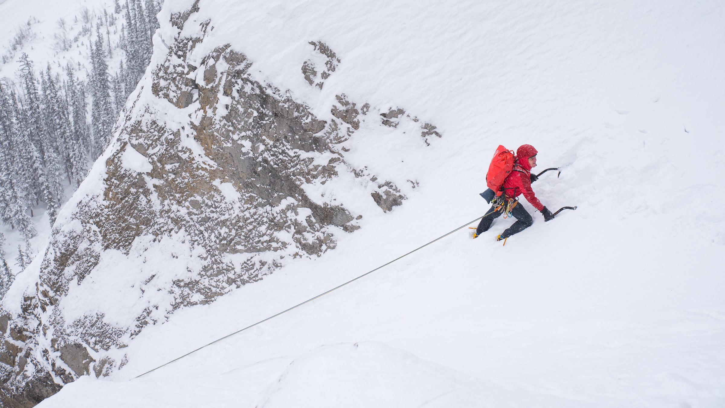 Ice climber ascends steep snow slope roped to his partner out of sight.