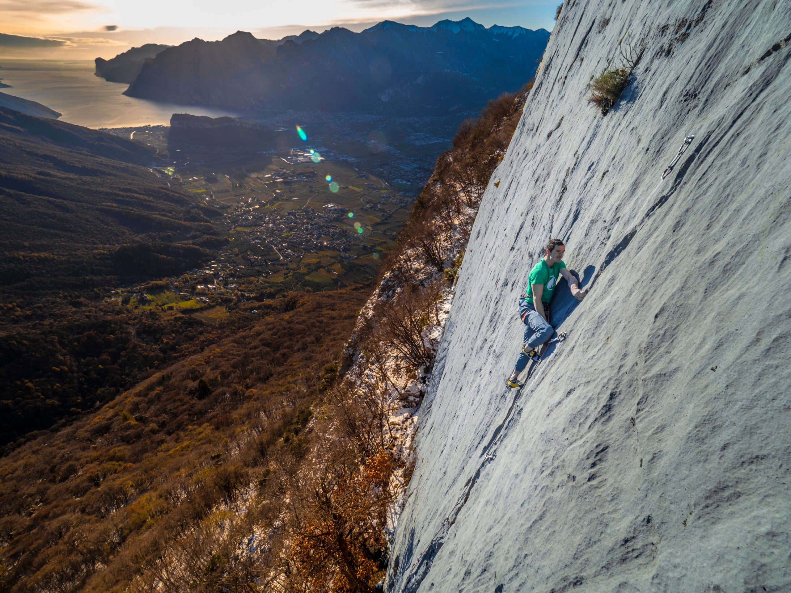 Adam Ondra climbing a slab route with Arco, Italy in the background